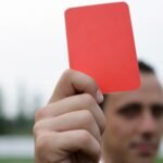 Close-up of a referee holding a red card, signaling a penalty in a soccer match.